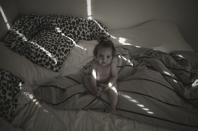 Portrait of baby girl sitting on bed at home