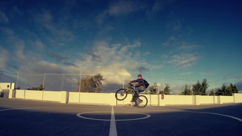 Side view of man doing wheelie on footpath against sky