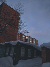 Snow covered houses by building against sky at dusk