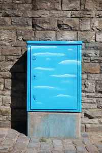 Blue metallic electric box against stone wall