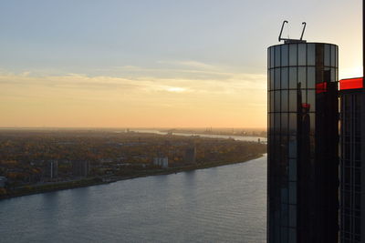 River amidst buildings in city against sky during sunset