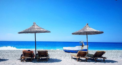 Deck chairs on beach against clear blue sky