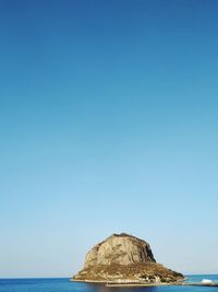 Rock formation in sea against clear blue sky