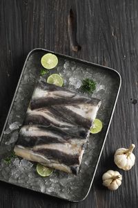 Top view frozen catfish fillet lele with ice and sliced lime, on wooden table. selected focus