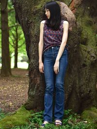 Full length of woman standing by tree trunk in forest