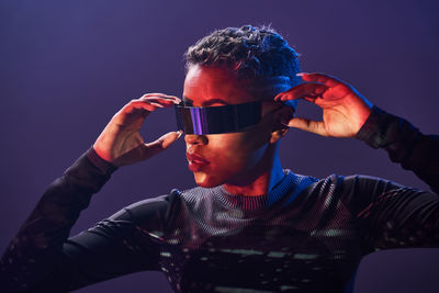 African american martial female with short hair in trendy vr goggles standing on purple background with outstretch arms in studio