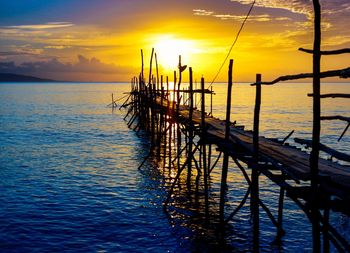 Silhouette wooden posts in sea against sky during sunset