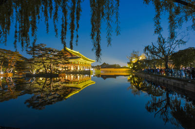 Illuminated building by lake against sky at night