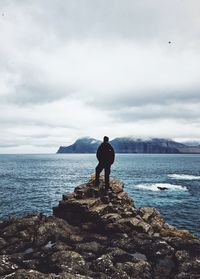 Rear view of man standing on rock by sea against sky