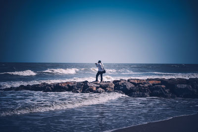 Man standing on rocks by sea against clear sky