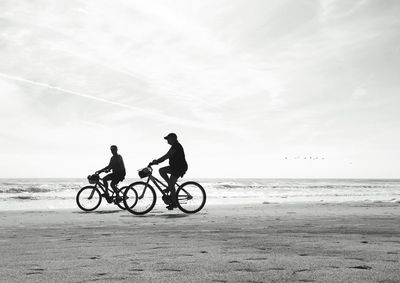 People riding bicycle on beach against sky