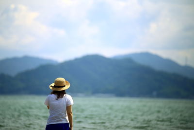 Rear view of woman standing by river against sky