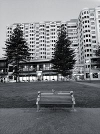 Empty park bench by building in city against sky