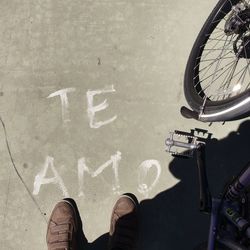 Low section of man standing with bicycle by text on footpath