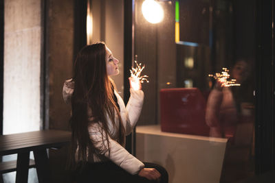 Woman holding illuminated lighting equipment while sitting at restaurant