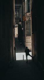 Rear view of silhouette man walking on street amidst buildings