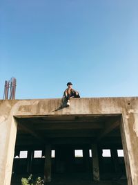 Low angle view of man standing by building against clear blue sky