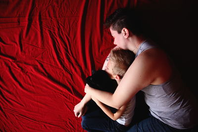 Mother embracing son while sleeping on red fabric