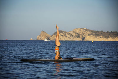 Female athlete exercising on paddleboard at sea against clear sky