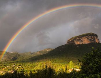 Scenic view of rainbow over mountain against dramatic sky