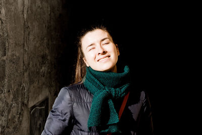 Young smiling woman wearing warm clothing by wall at night