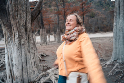 Portrait of a smiling young woman holding tree trunk