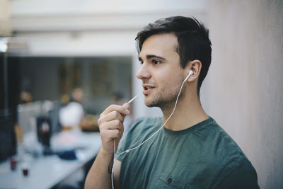 Young male computer programmer using in-ear headphones while talking in office