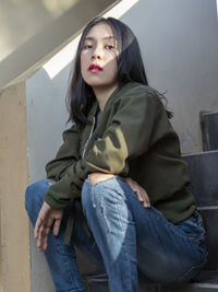 Portrait of a young woman sitting against wall