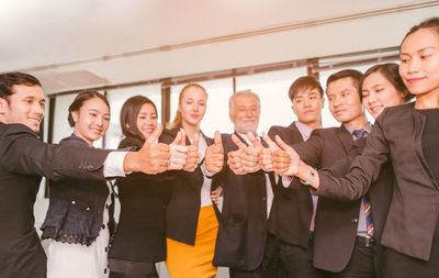 Business people showing thumbs up while standing in office