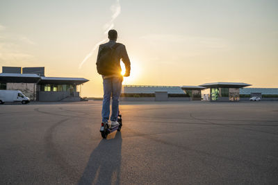 Businessman riding electric push scooter on street at sunset