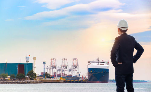 Rear view of man standing at harbor against sky