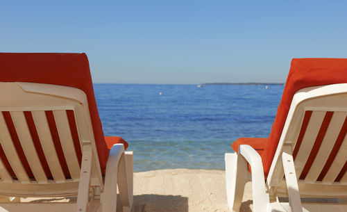 Scenic view of sea with chairs against clear blue sky