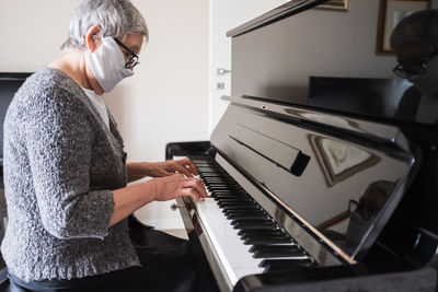  portrait of a senior woman with  face mask playing the piano at home. concept of resilience.