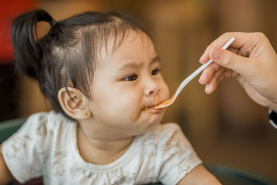 Cropped hand of person feeding girl at home