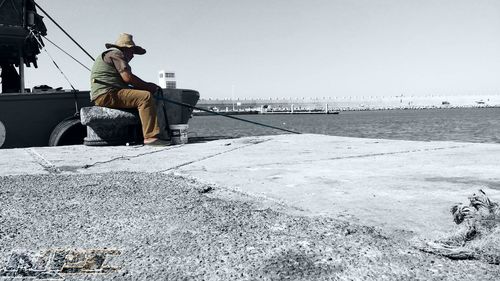 Rear view of man sitting on beach against clear sky