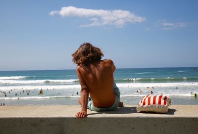 Rear view of shirtless boy on beach against sky