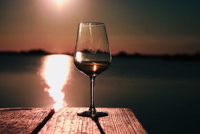 Wine glass on table against sea during sunset