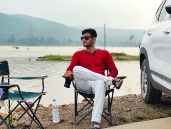 Young man sitting on chair at lakeshore