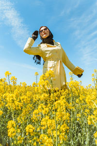 Portrait of woman standing amidst yellow flowering plants on field against sky