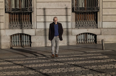 Adult man in suit crossing street against stone wall with sunlight and shadow