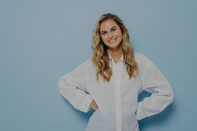 Portrait of young woman standing against blue background