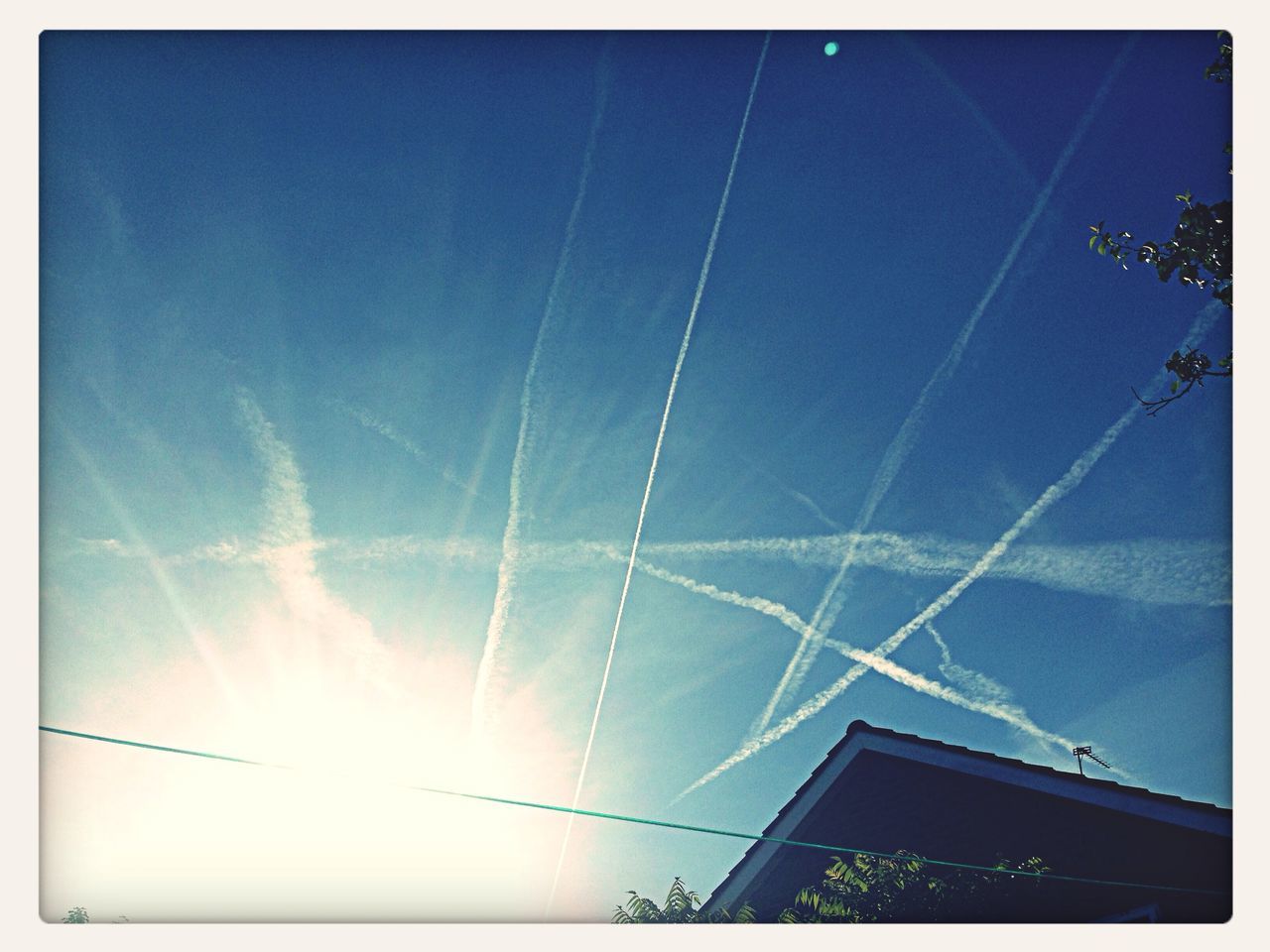 low angle view, transfer print, blue, sky, vapor trail, auto post production filter, building exterior, built structure, architecture, sunlight, sunbeam, sun, day, nature, cloud - sky, outdoors, no people, high section, lens flare, beauty in nature