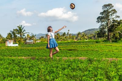 Woman throwing hat while standing at farm