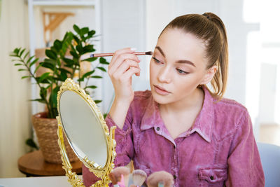 Make-up at home. young beautiful woman with makeup brush applies eye shadow