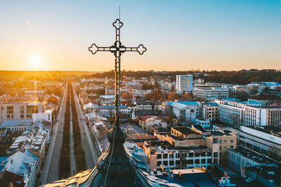 Cross on tower against cityscape at sunset