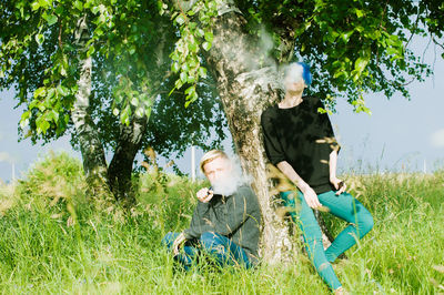 Friends smoking while by tree on field