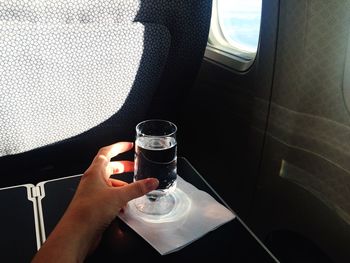Cropped hand reaching for drinking glass by airplane window
