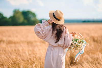 Rear view of woman holding flower standing on field