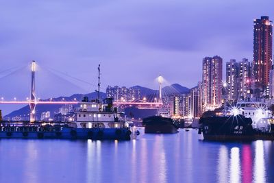 Illuminated city by river against sky at dusk