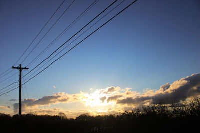 Low angle view of silhouette electricity pylon against sky during sunset